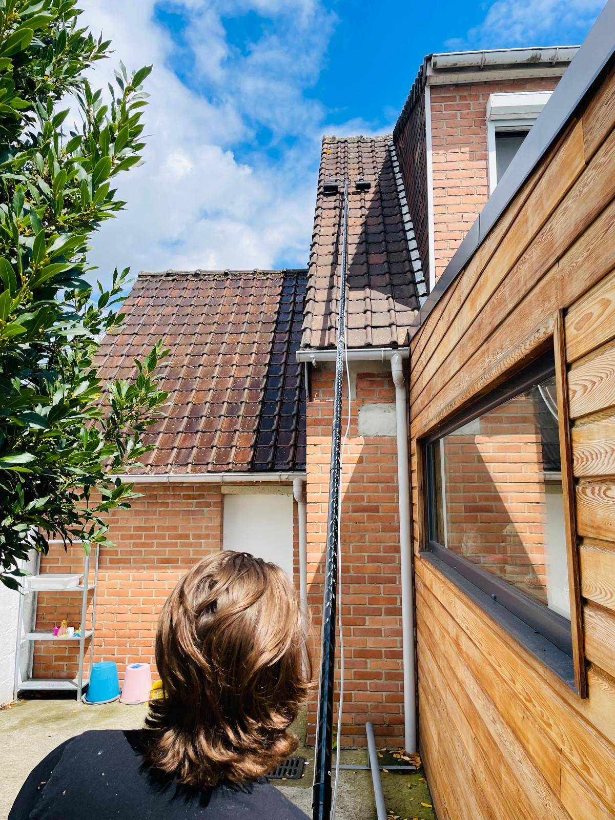 Perche télescopique de démoussage déployée le long d'une façade de maison